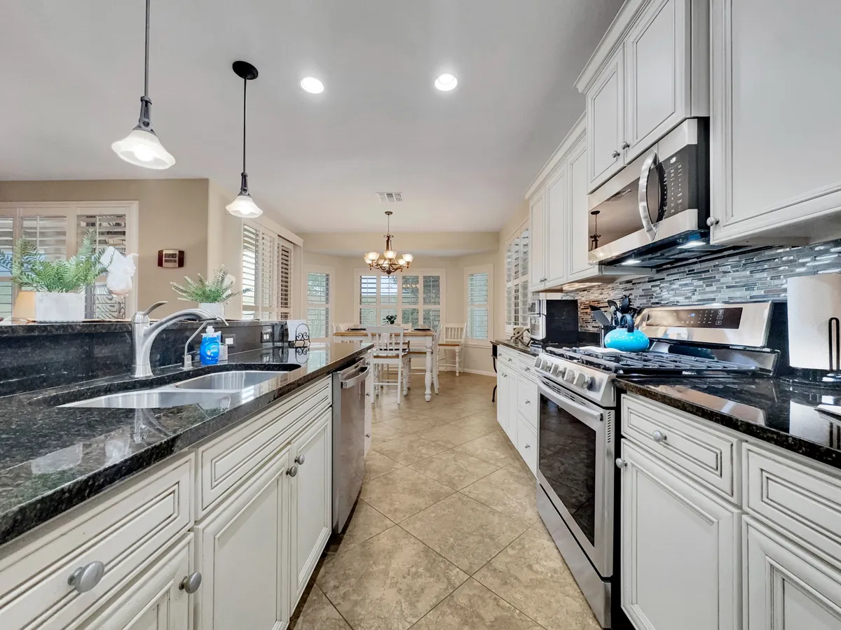A spacious kitchen area with gleaming granite countertops, up-to-date appliances, and an adjacent dining area crowned by a stylish chandelier. The warm and inviting mood highlights the heart of the home, where cooking and memorable meals come together.