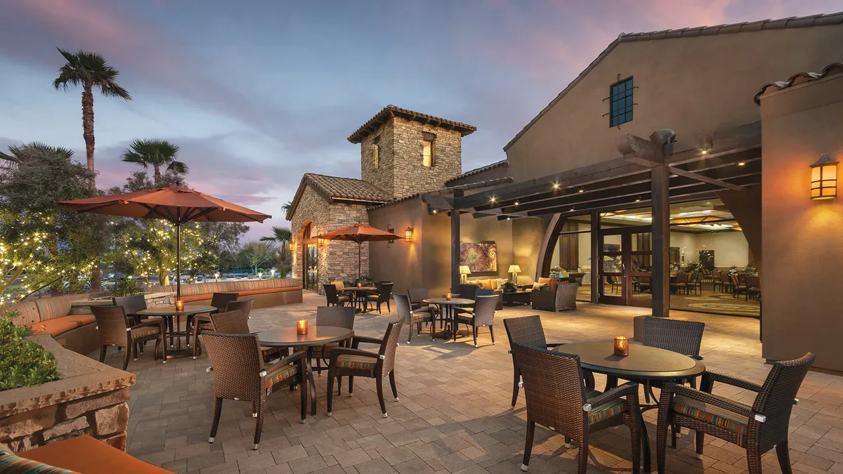 An elegant outdoor seating area with table candles set against a stone building, surrounded by palm trees and bathed in the soft light of sunset. The space is ideal for dining, socializing, or relaxing while enjoying peaceful views.