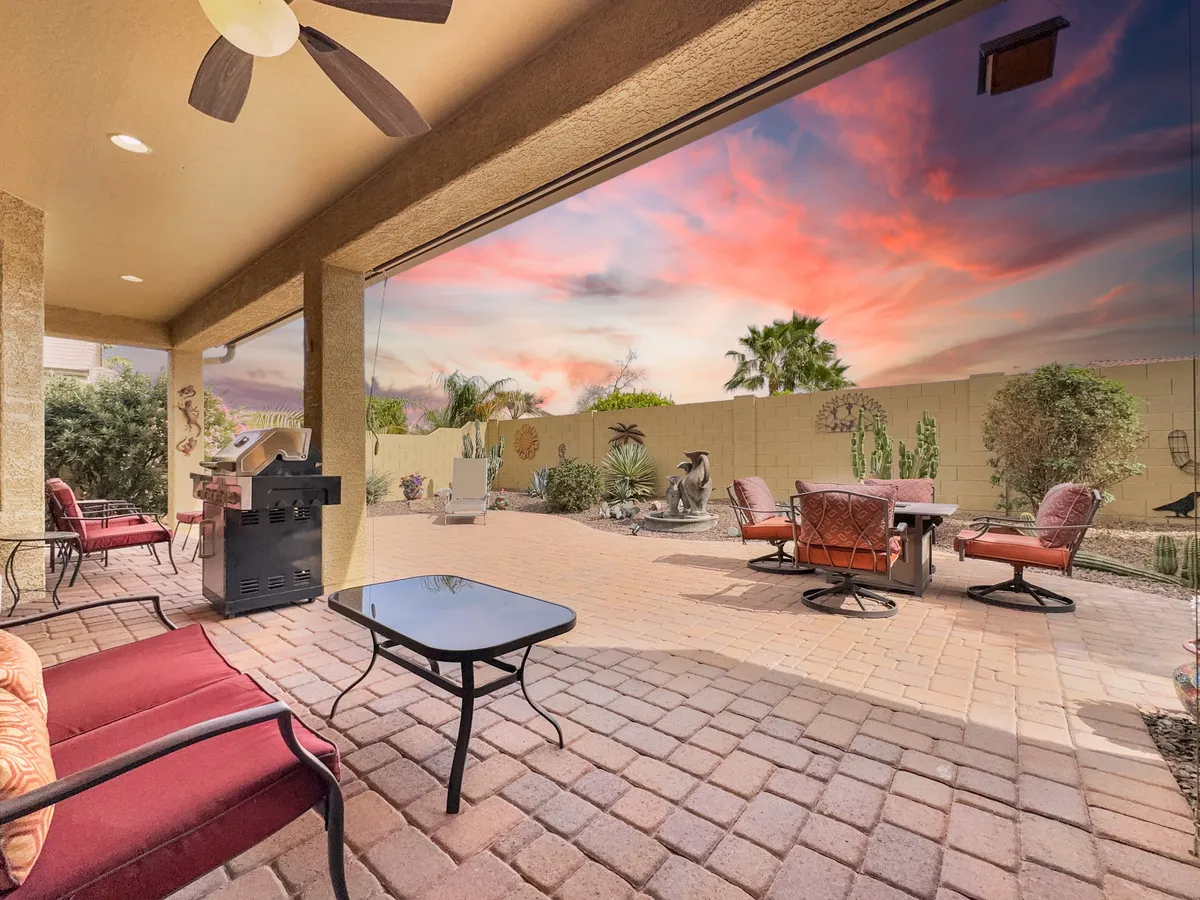 An outdoor patio with a dining table, comfortable seating, grill, and lush landscaping set beneath the Arizona sky. The mood is relaxed and social, perfect for al fresco dining and sunset gatherings.