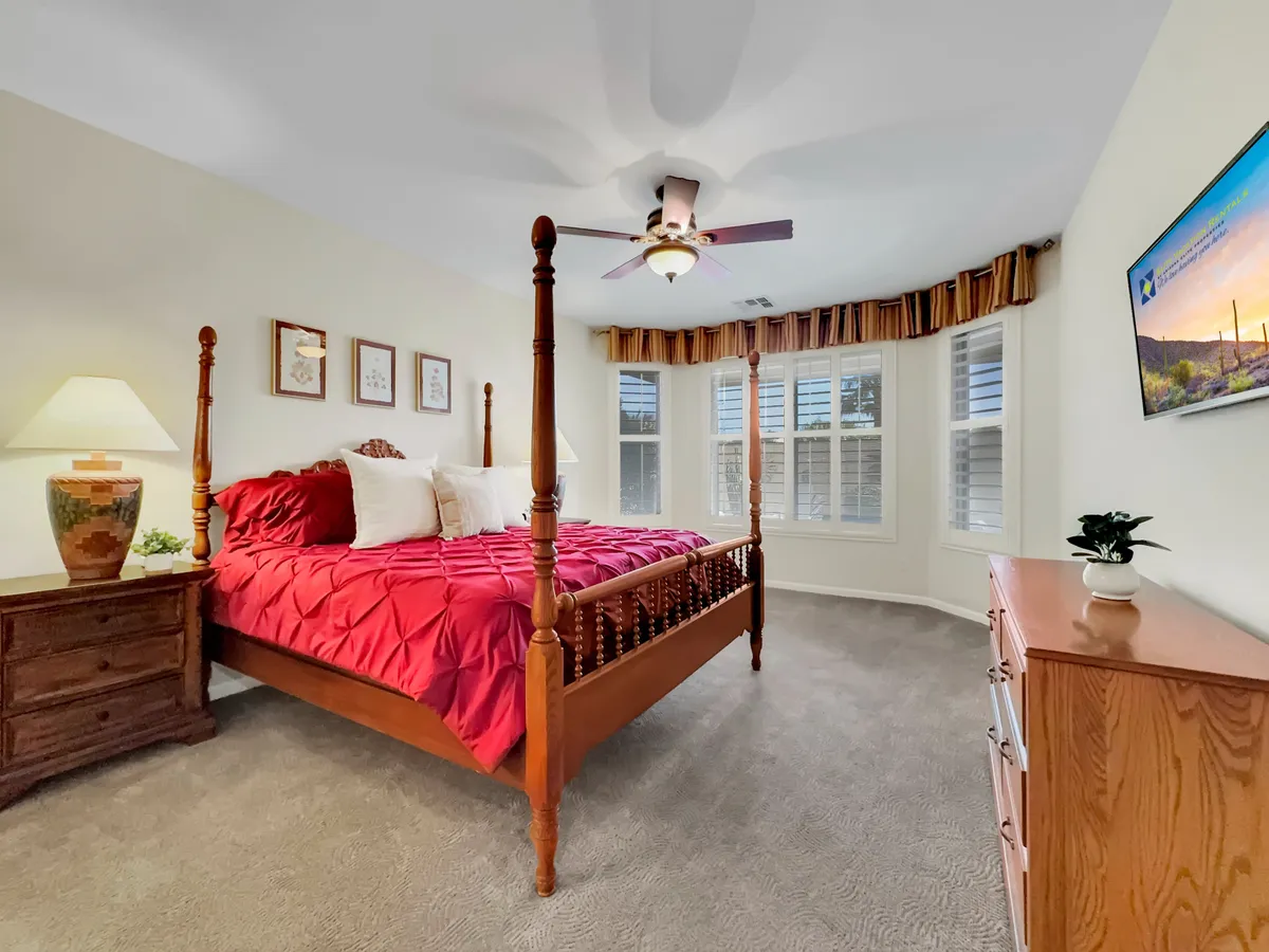 A serene bedroom with a four-poster bed, decorative lamp, framed artwork, a TV atop a dresser, and soft bedding. The space feels private, inviting, and perfect for unwinding after a long day.