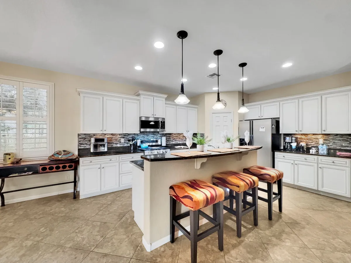 A bright, modern kitchen featuring an island countertop with colorful bar stools and sleek, contemporary appliances. The space is lively and well-appointed, creating a welcoming environment for cooking and entertaining.