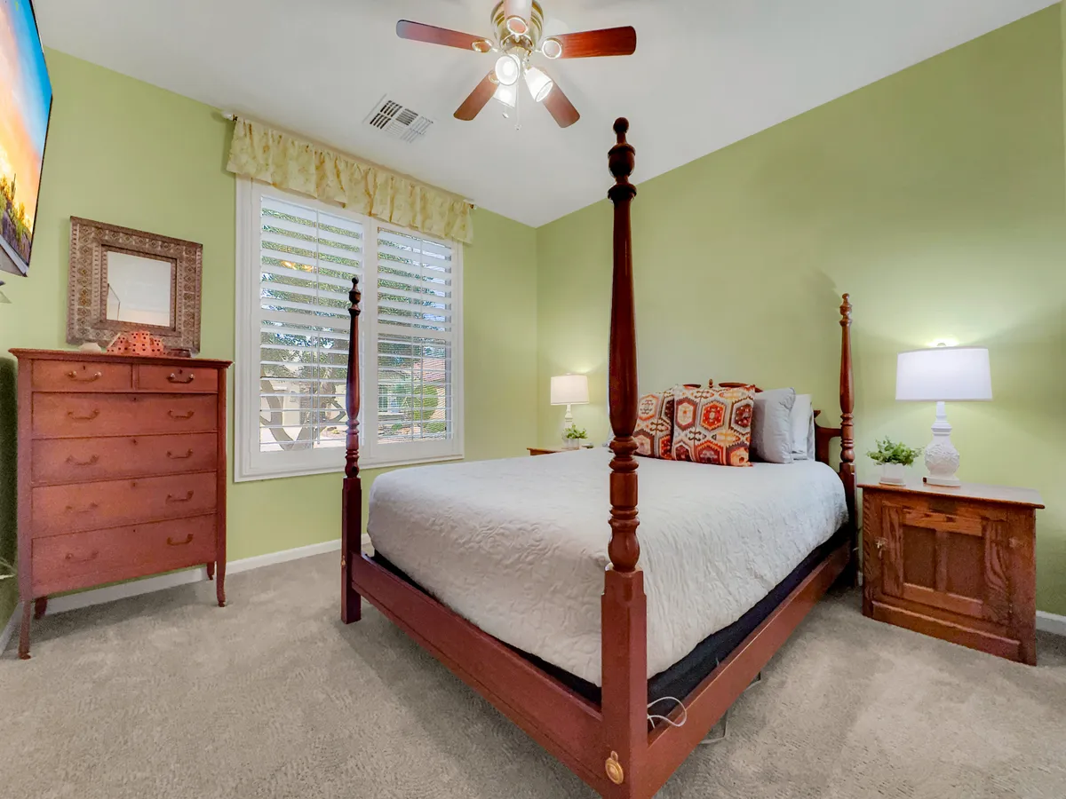 Another inviting bedroom featuring a four-poster bed, wooden dresser, decorative pillows, and lamps, bathed in natural light. The cozy arrangement signals comfort and relaxation, ideal for a guest or secondary bedroom.
