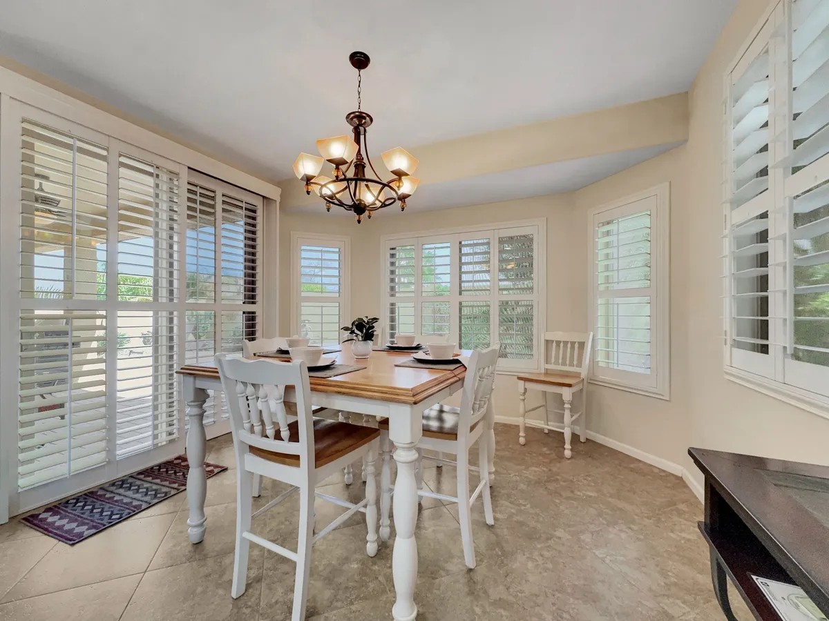 A sunlit dining room with a spacious table, elegant chandelier, and large windows with shutters. The setting is cozy yet sophisticated, ideal for hosting dinners or enjoying everyday meals with family and friends.