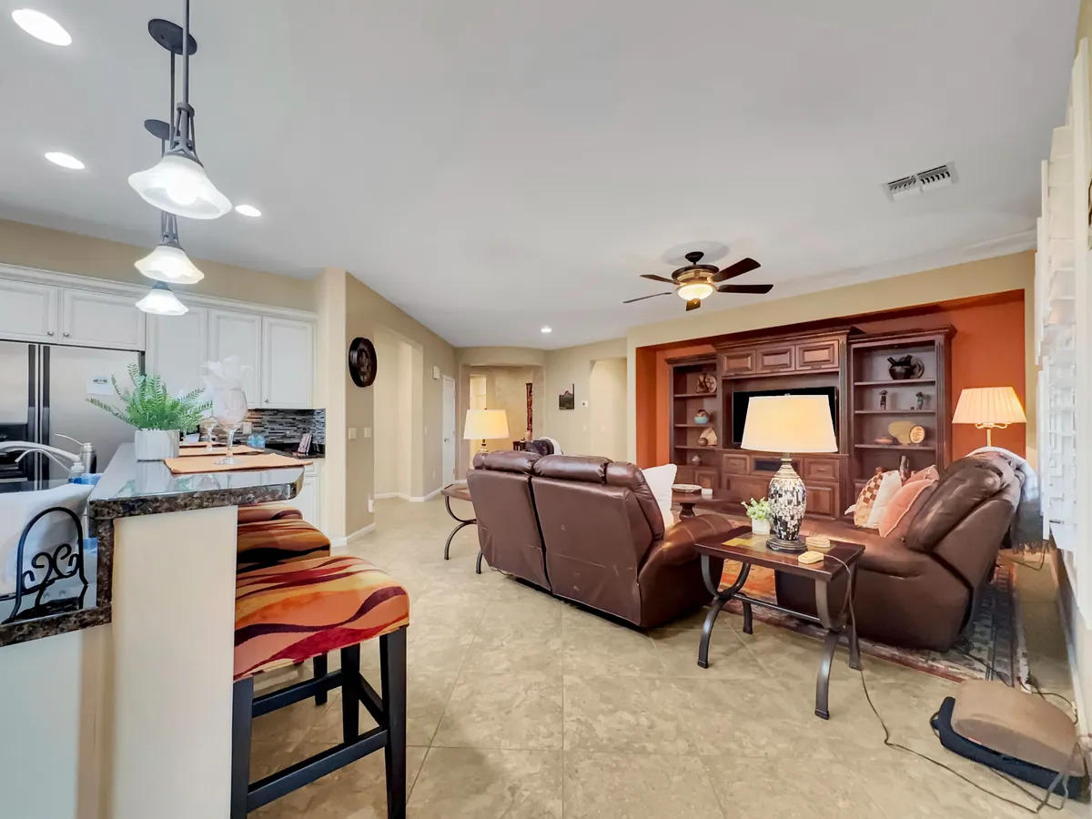 Comfortable leather sofas are arranged around a stylish coffee table and a decorative shelving unit, creating an inviting space for family gatherings, board games, or casual conversation. Soft lighting and layered textures enhance the cozy mood.