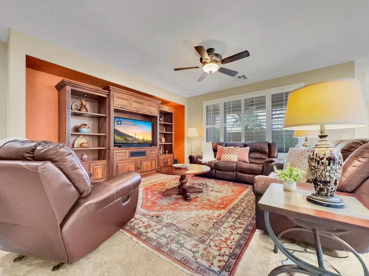 A cozy living area spotlighting reclining leather chairs, a wooden entertainment center with a mounted Smart TV, and a round coffee table atop a decorative rug. The atmosphere is intimate yet accommodating, ideal for unwinding, watching TV, or enjoying a book.