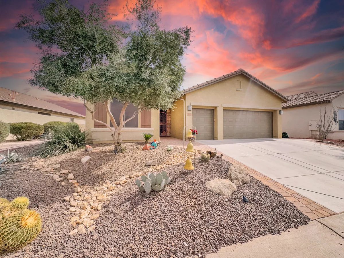 This image features a welcoming front yard with carefully maintained landscaping, garage doors, and a clear view of the entryway adorned with desert elements such as cacti and rocks. The setting suggests a tranquil, community-oriented neighborhood perfect for seasonal living.